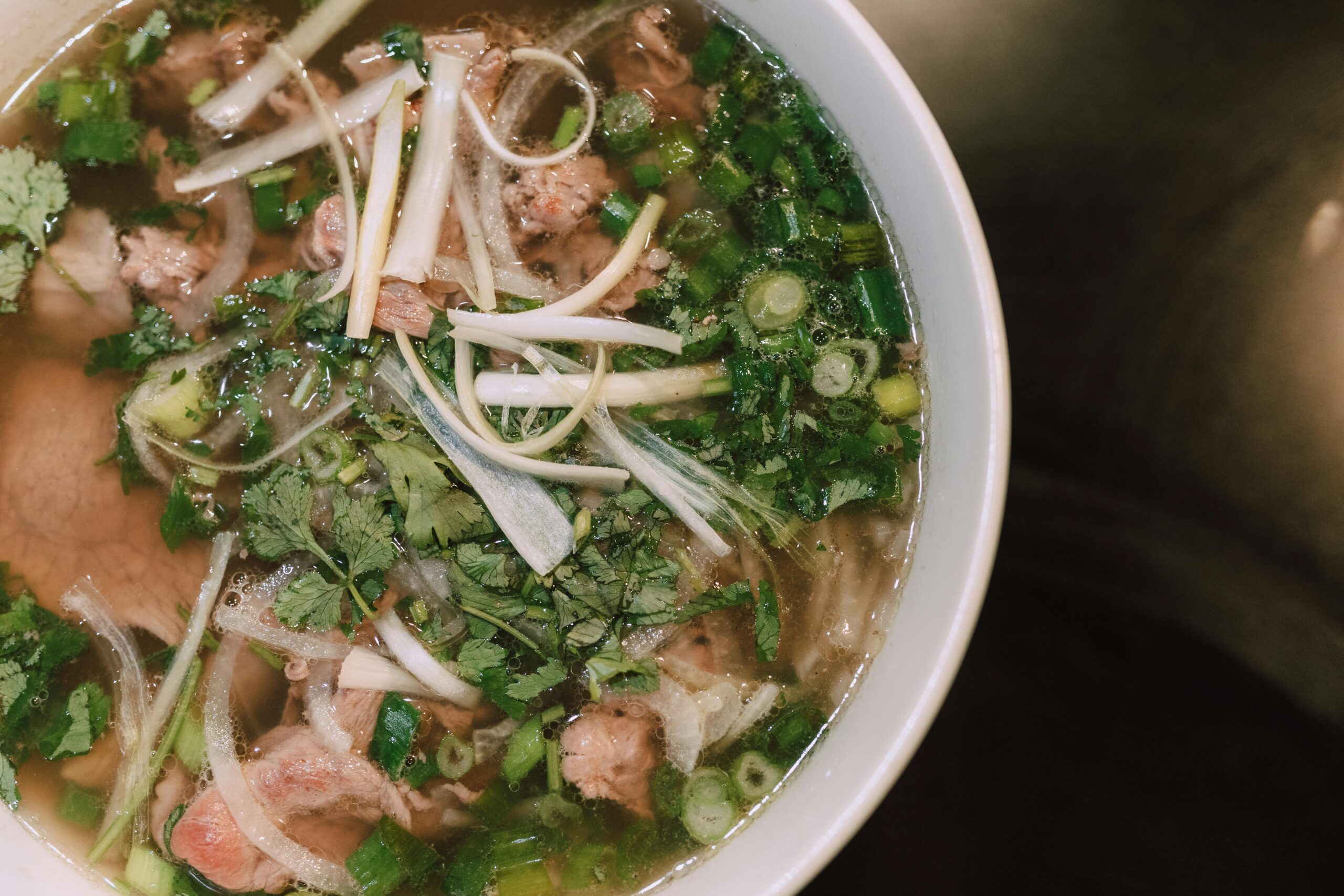 Delicious Vietnamese Pho noodle soup with fresh herbs and beef, captured from above.